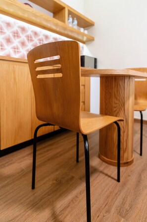 A wooden chair with a backrest and seat, positioned in front of a wooden table and a kitchen counter. - Don Manuel - Luxury Apartments & Studios (Oaxaca)