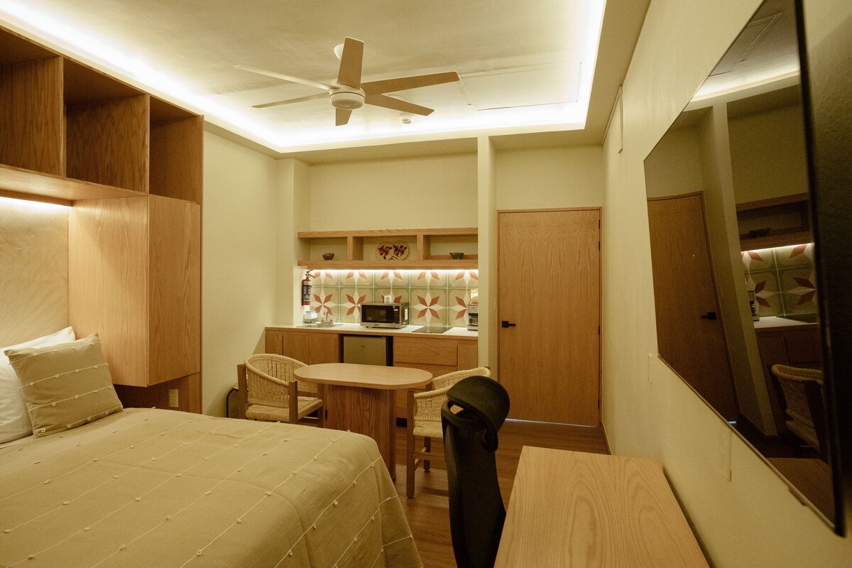 A hotel room with a bed, a desk, a chair, a microwave, and a ceiling fan.