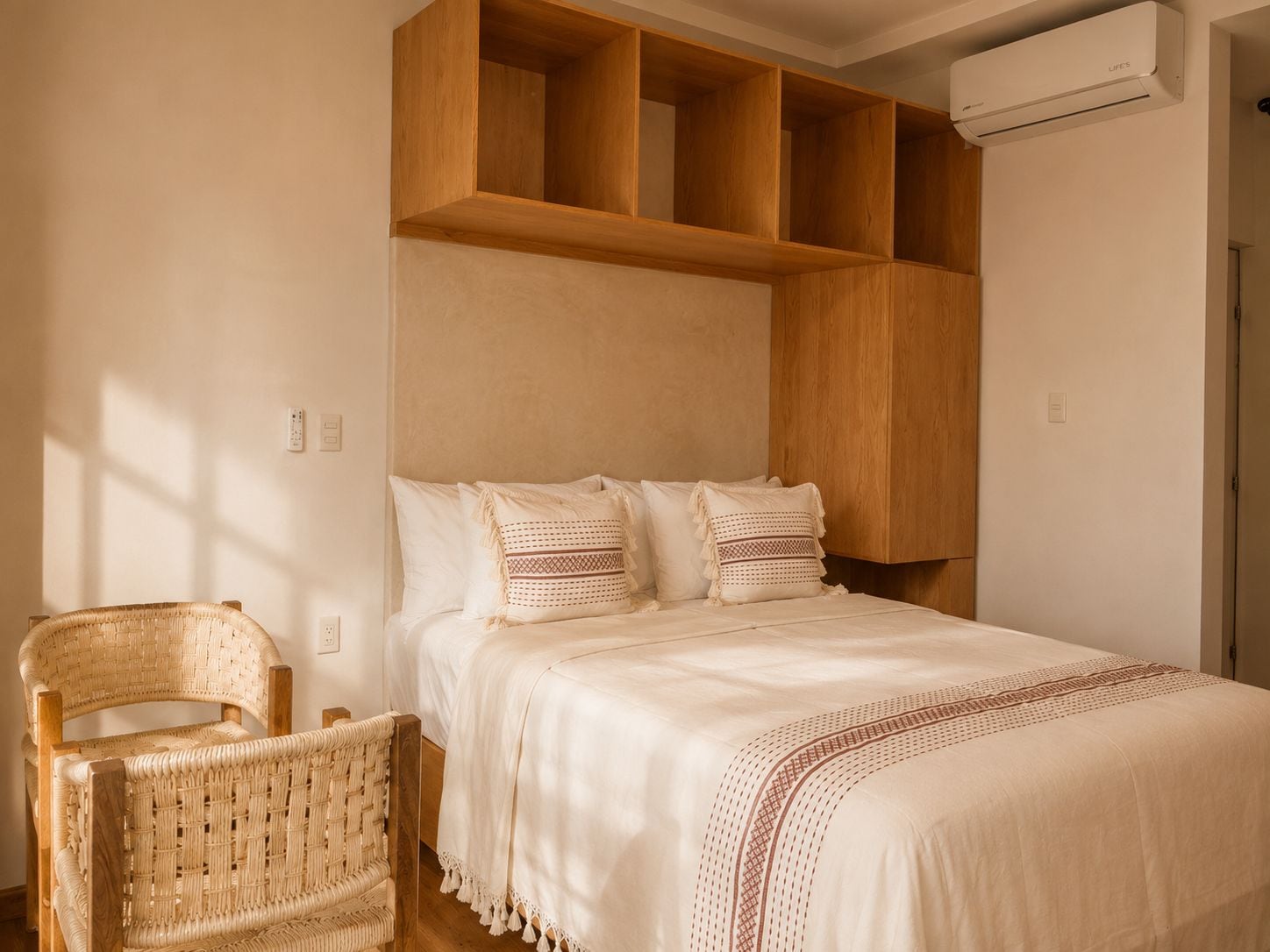 Un dormitorio con cama, cabecera de madera, una silla de mimbre y un equipo de aire acondicionado.