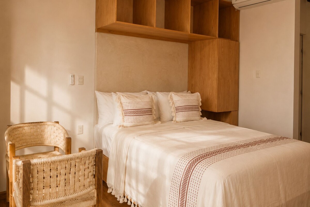 A bedroom with a bed, a wooden headboard, a wicker chair, and an air conditioning unit.