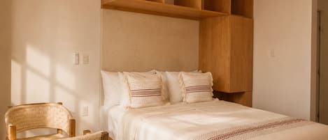 A bedroom with a bed, a wooden headboard, a wicker chair, and an air conditioning unit.
