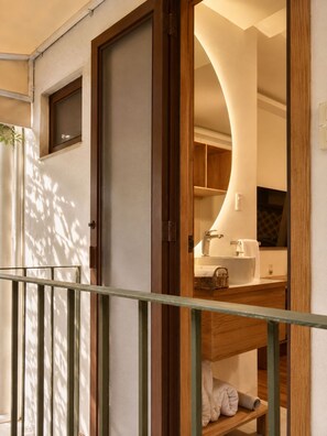 A hotel room with a wooden door, a small window, a bathroom with a sink and mirror, and a shelf with towels. - Don Manuel - Luxury Apartments & Studios (Oaxaca)