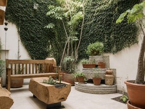 A courtyard with a wooden bench, potted plants, and a wall covered in ivy. - Don Manuel - Luxury Apartments & Studios (Oaxaca)