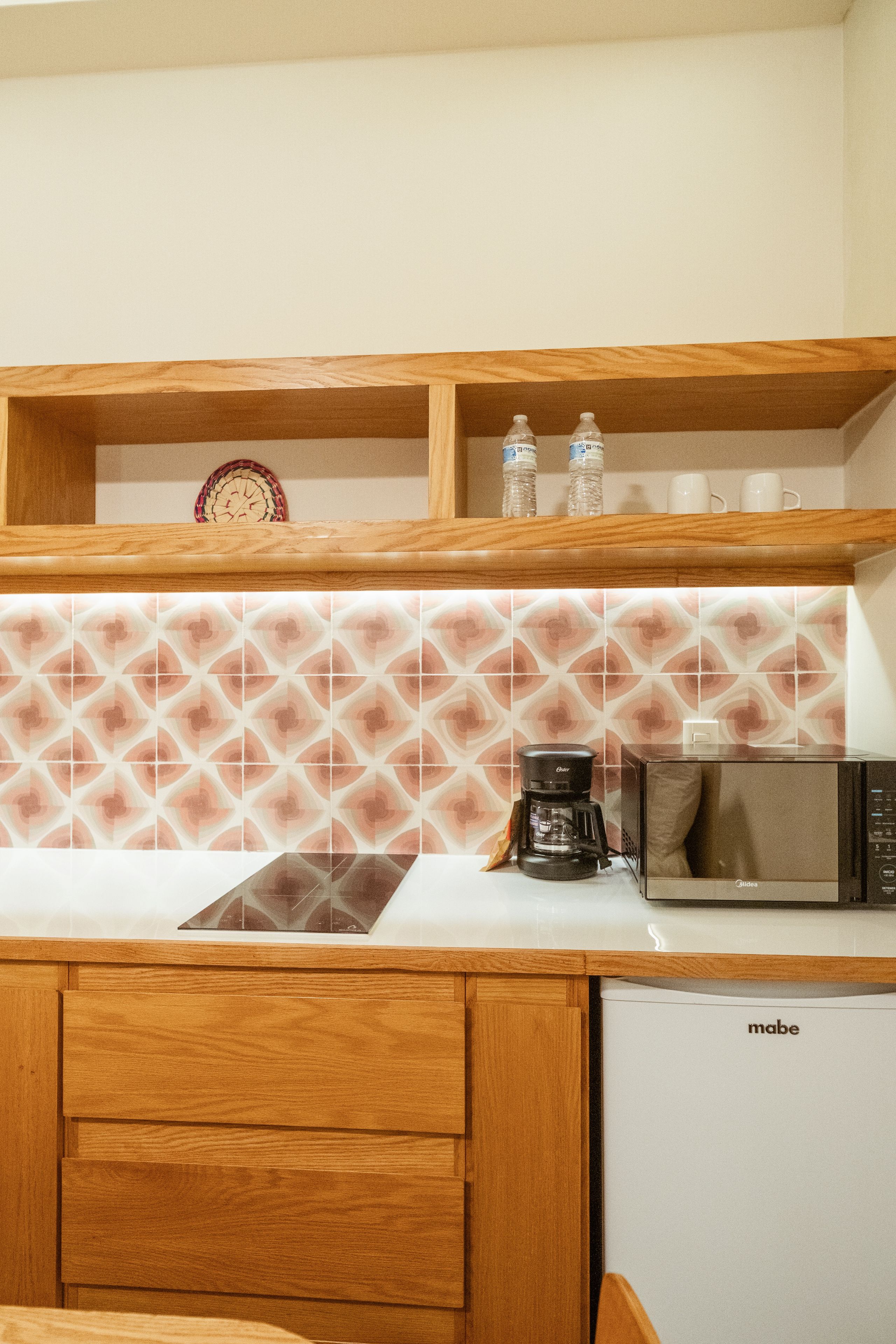 Una cocina con microondas, cafetera y una repisa con botellas y un reloj.