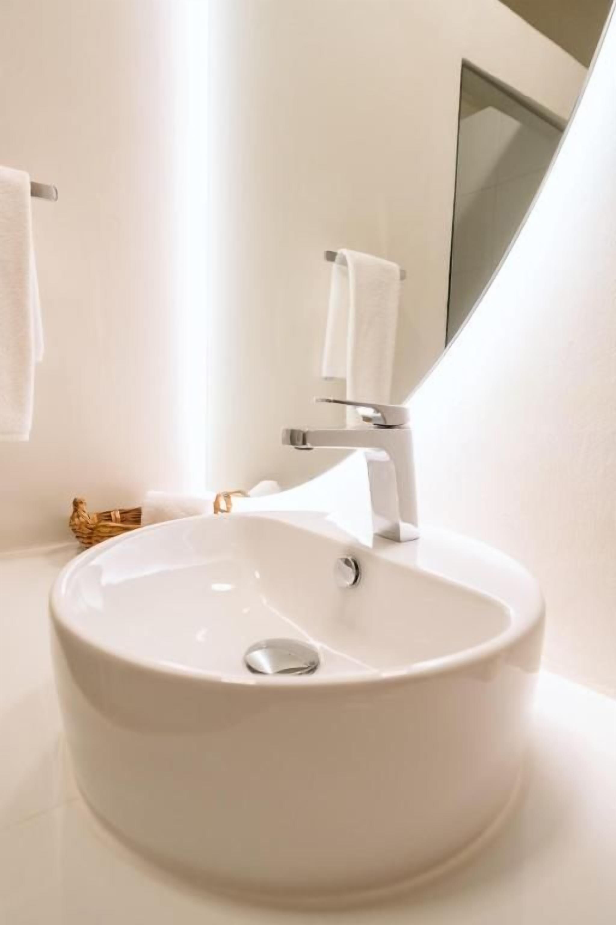 Un baño blanco con un lavabo redondo, un perchero y un espejo.