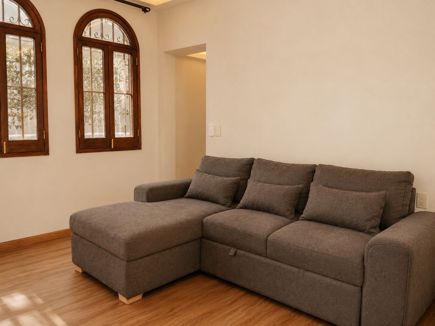 Un sofá modular en una habitación con suelo de madera y dos ventanas arqueadas.