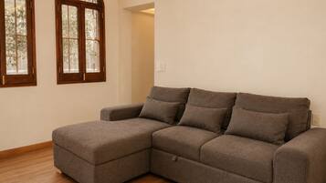 Un sofá modular en una habitación con suelo de madera y dos ventanas arqueadas.