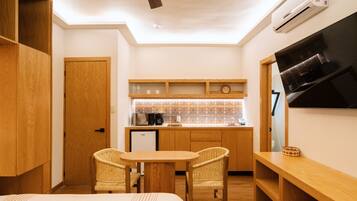 Una habitación de hotel compacta con kitchenette, un comedor con dos sillas de mimbre, una cama y un ventilador de techo.