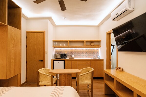 A compact hotel room with a kitchenette, a dining area with two wicker chairs, a bed, and a ceiling fan. - Don Manuel - Luxury Apartments & Studios (Oaxaca)