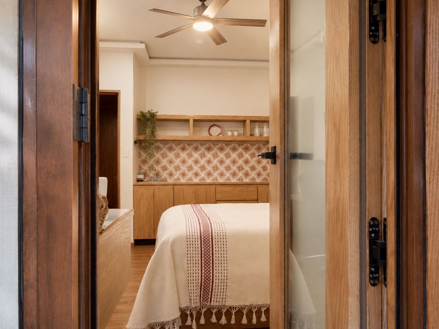 Un dormitorio con cama, ventilador de techo y una kitchenette al fondo.