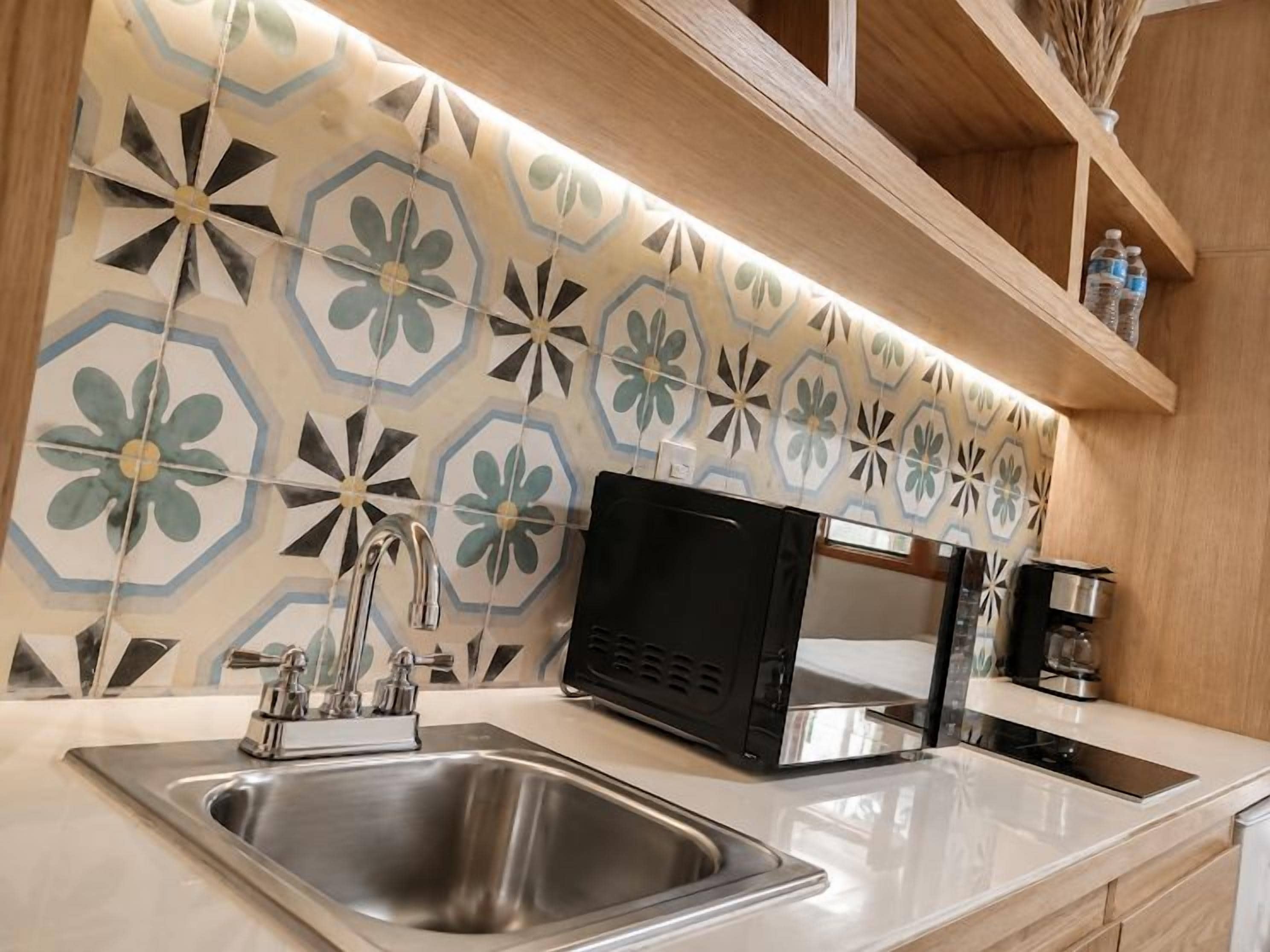 Una cocina con un lavamanos de acero inoxidable, un microondas negro y un salpicadero con diseño.