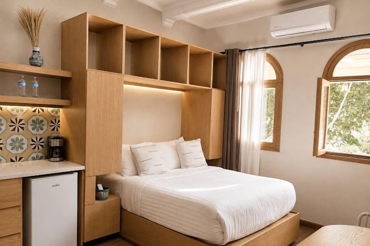 A bedroom with a bed, built-in shelving, a small desk, and a window.