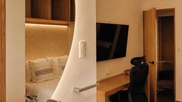A modern hotel room with a curved wall, a large bed, a desk with a chair, a television, and a bathroom with a sink and mirror.