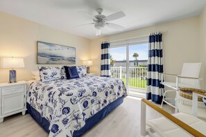 Ein Schlafzimmer mit Bett, Deckenventilator, Nachttisch, Lampe, Gemälde und Blick ins Freie.