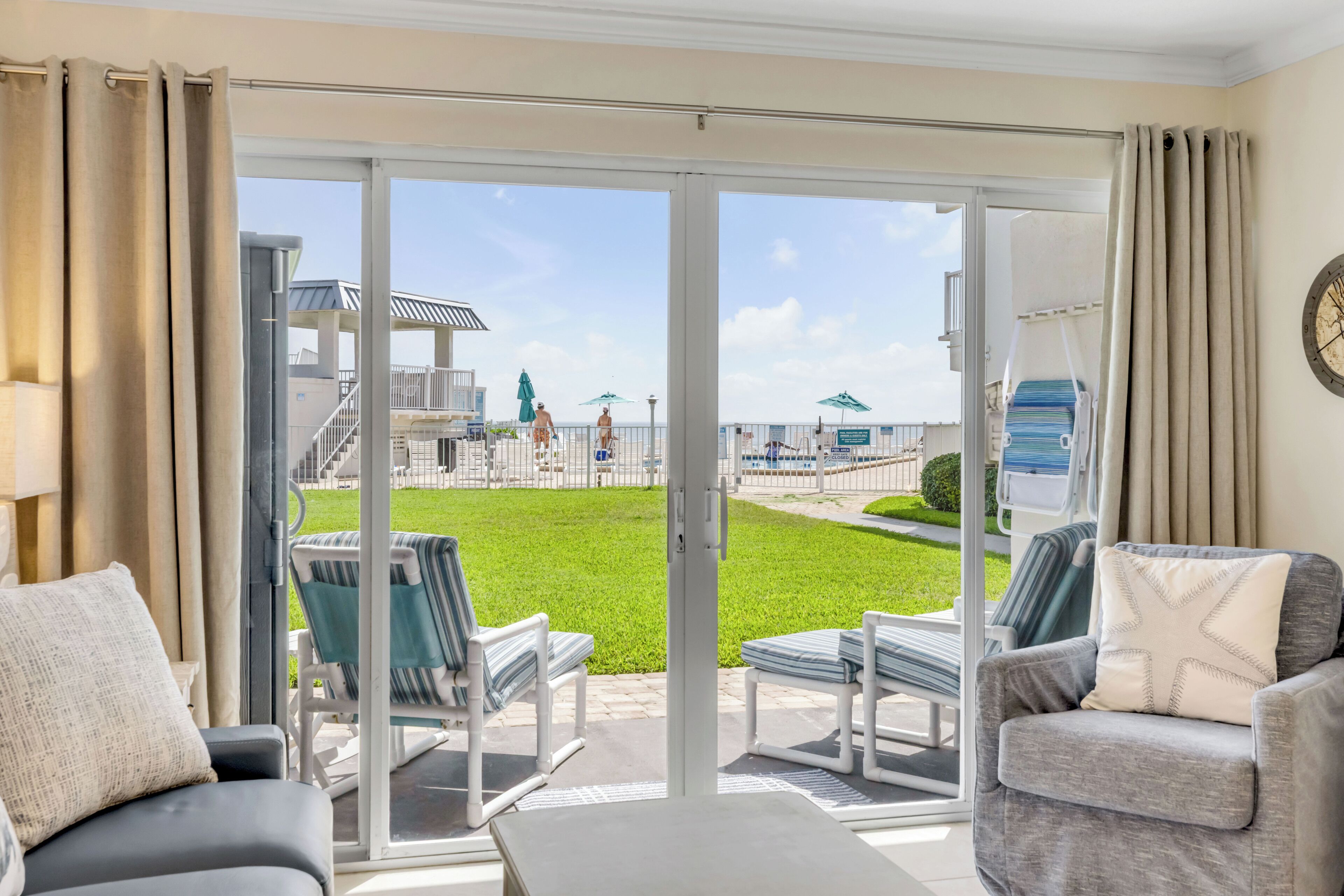 A hotel room with a sliding glass door leading to an outdoor area with a pool, lounge chairs, and a children's play structure.