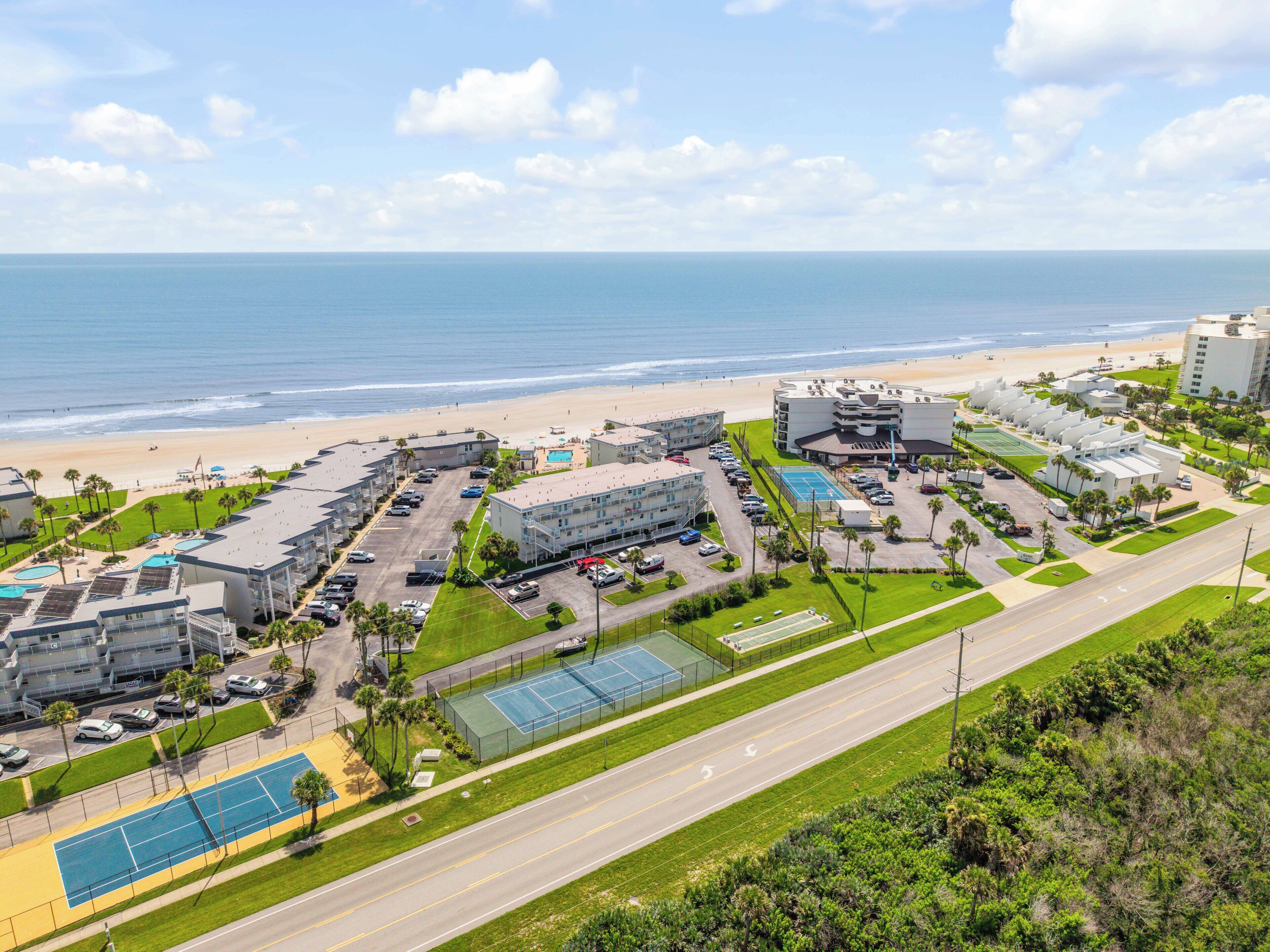 An aerial view of a coastal hotel with multiple buildings, a beach, and a tennis court.