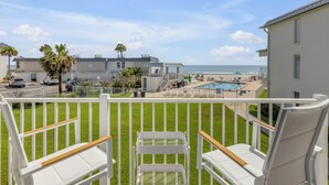 Un balcone con vista su piscina e spiaggia, sedie bianche e un'area recintata.