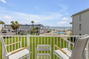 Ein Balkon mit Blick auf Pool und Strand, weiße Stühle und ein eingezäunter Bereich.