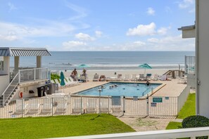 Ein Poolbereich mit Blick auf den Strand, Liegestühle und ein Rettungsschwimmerstand.