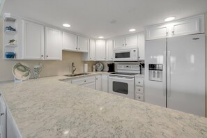 Una cocina con armarios blancos, un microondas, una estufa y un refrigerador.