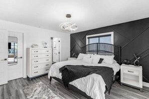 A modern bedroom with a bed, dresser, nightstand, and a unique ceiling light fixture. - Canal-Front 3BR Retreat with Amazing Pool & Coastal Charm (Saint James City)