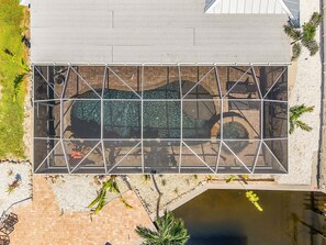 An aerial view of a building with a large glass enclosure, a brick pathway, and a small pond. - Canal-Front 3BR Retreat with Amazing Pool & Coastal Charm (Saint James City)