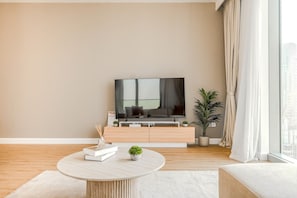 A modern living room with a flat-screen TV, a minimalist sofa, a coffee table, and a potted plant. - HAVN - 2 Bed in Downtown with Sea View (Dubai)