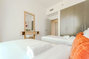 A hotel room with two beds, a wooden bedside table, a mirror, and a wardrobe. - HAVN - 2 Bed in Downtown with Sea View (Dubai)