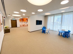 A spacious room with a carpeted floor, a large window with curtains, a flat-screen TV mounted on the wall, and a table with chairs. - HAVN - 2 Bed in Downtown with Sea View (Dubai)