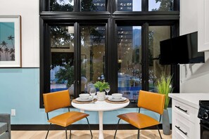 A modern kitchen with a dining table, two chairs, a TV, and a view of the city through large windows. - Petco Park Proximity | Urban Downtown Suite (San Diego)