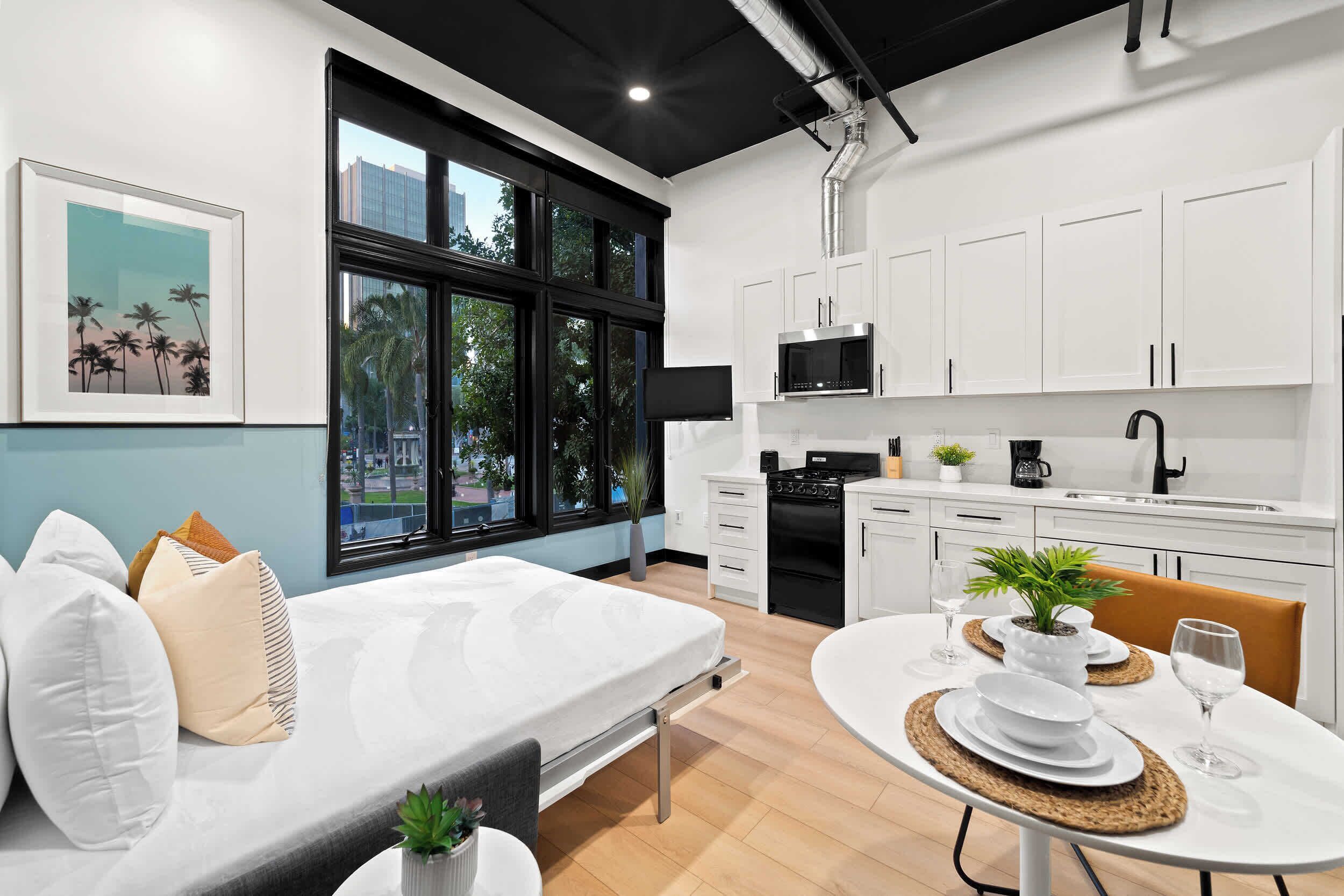 A modern kitchen with white cabinets, a black stove, and a window with a city view.