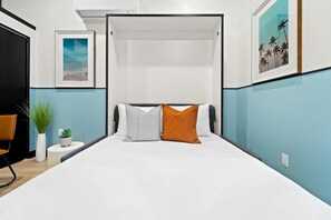 A bedroom with a bed, a bedside table, a chair, and a potted plant. - Petco Park Proximity | Urban Downtown Suite (San Diego)