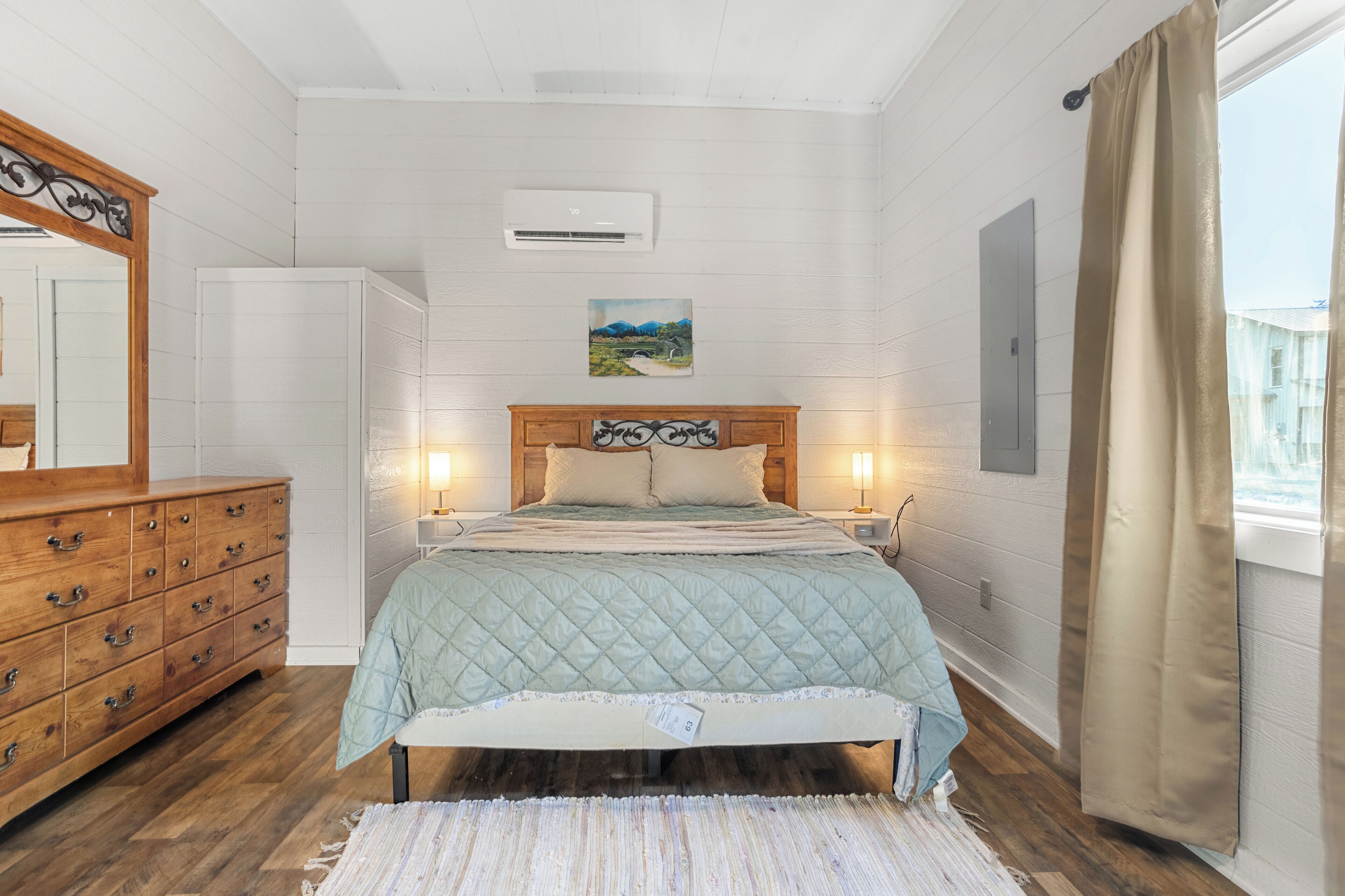 Een slaapkamer met een bed, een houten dressoir en een grote spiegel.