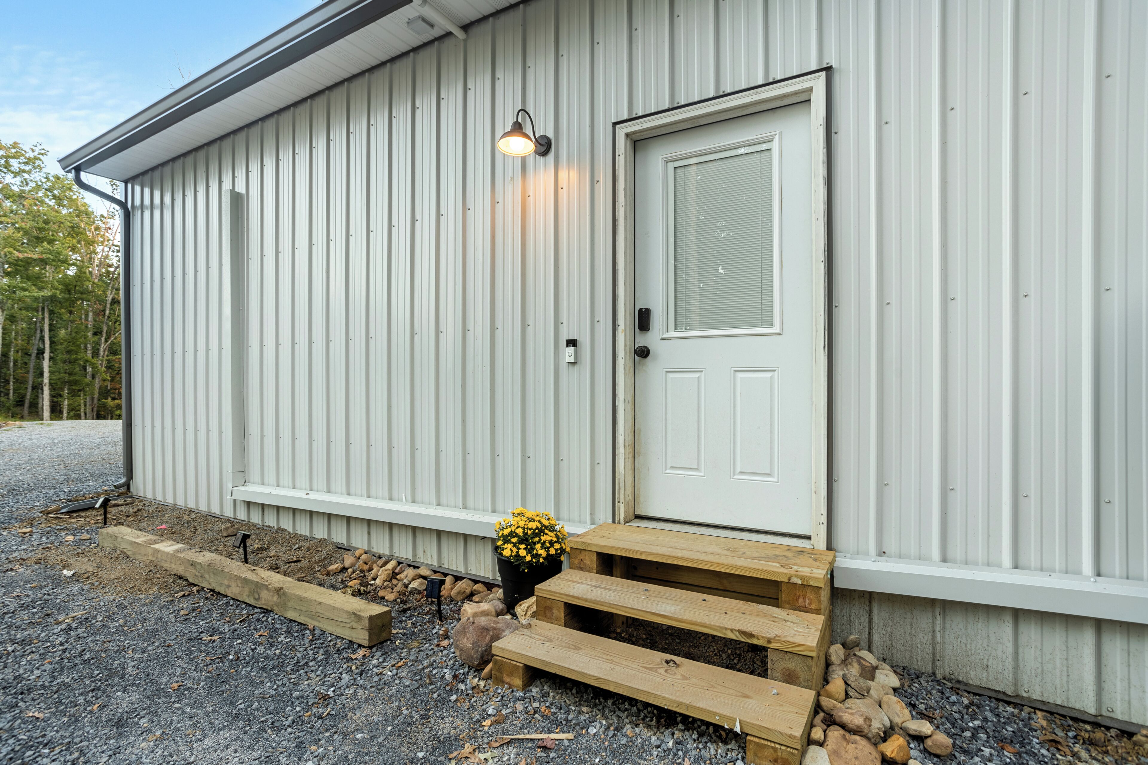 A building with a white exterior, a door with a window, and a small porch area with steps and a planter with yellow flowers.