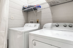 A laundry room with two white washing machines, a shelf with laundry items, and a wall-mounted electrical outlet.