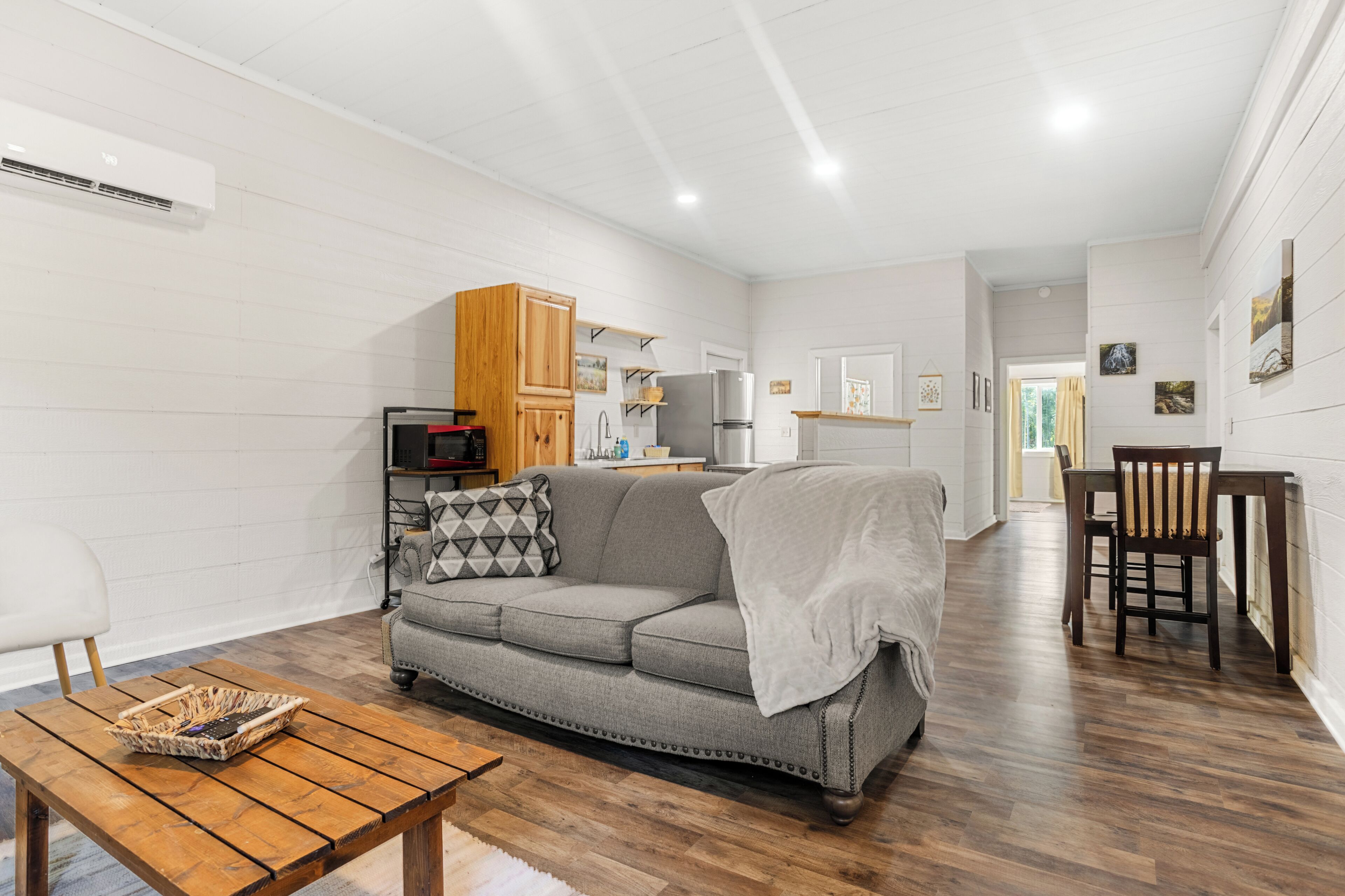 A modern living room with a grey sofa, wooden coffee table, and a kitchen area in the background.
