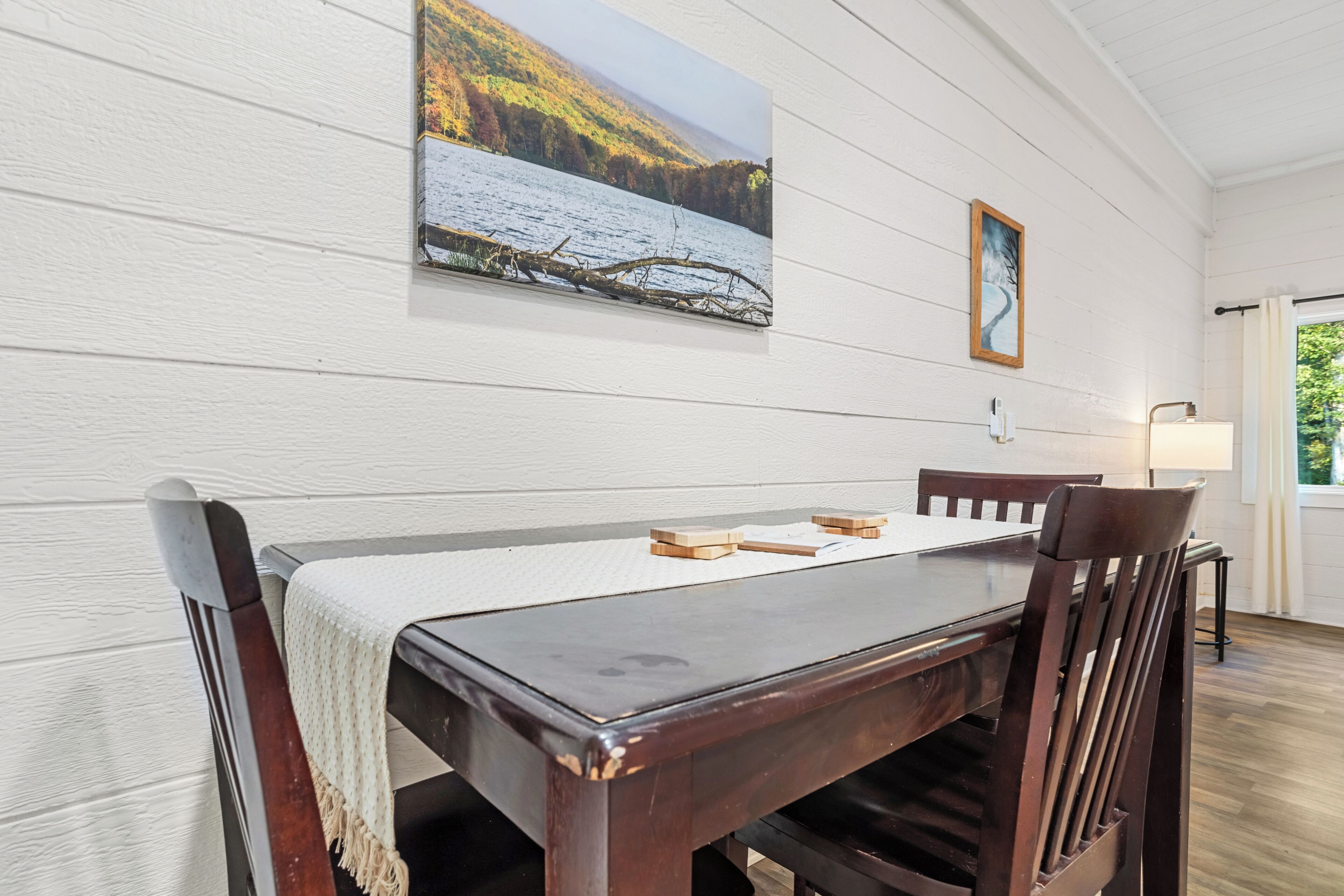 A dining area with a wooden table and chairs, a white tablecloth, and artwork on the walls.