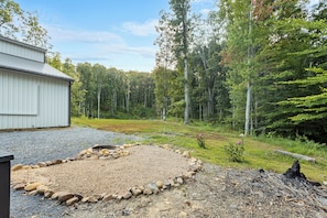 A gravel area with a stone border, surrounded by a forest and a building.