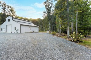 A large, single-story building with a gravel driveway and a forested area in the background.
