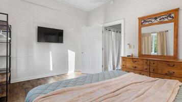 Un dormitorio con cama, cómoda, televisor montado en la pared y puerta que da a otra habitación.