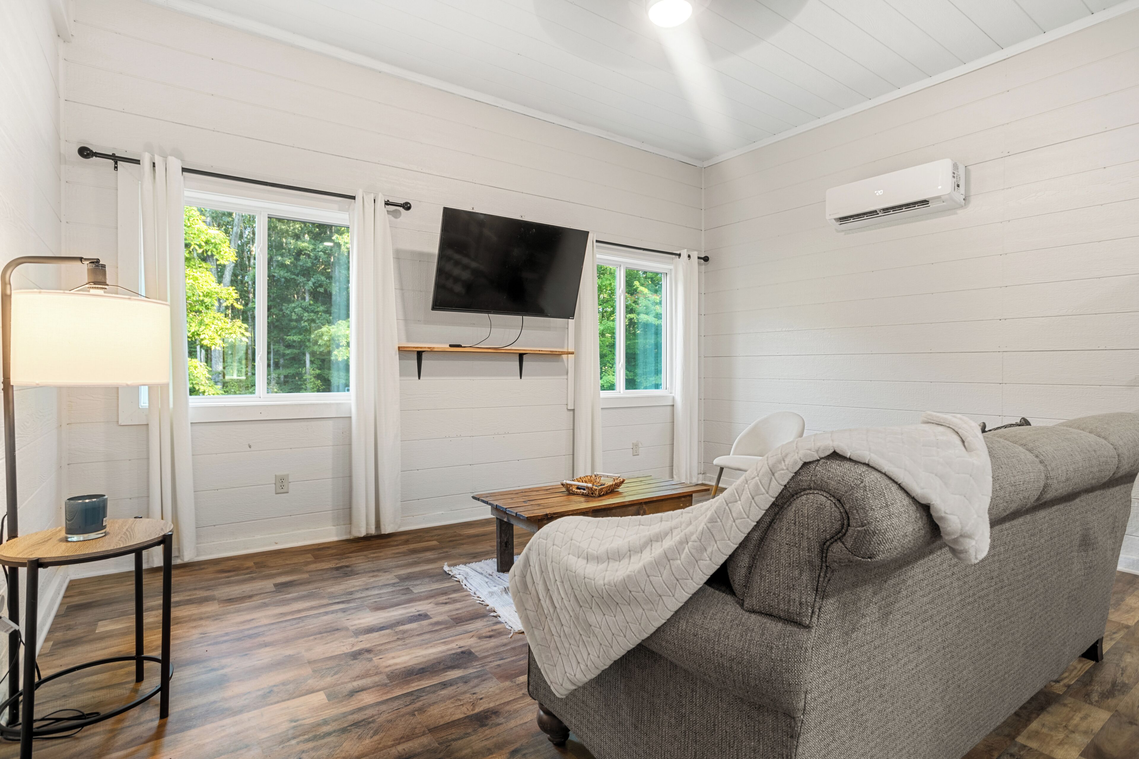 Una habitación con sofá, televisión, lámpara y ventana con cortinas.