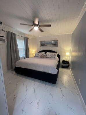 A bedroom with a bed, a ceiling fan, a nightstand, a lamp, and a window with curtains. - “No pasa nada” (Pompano Beach)