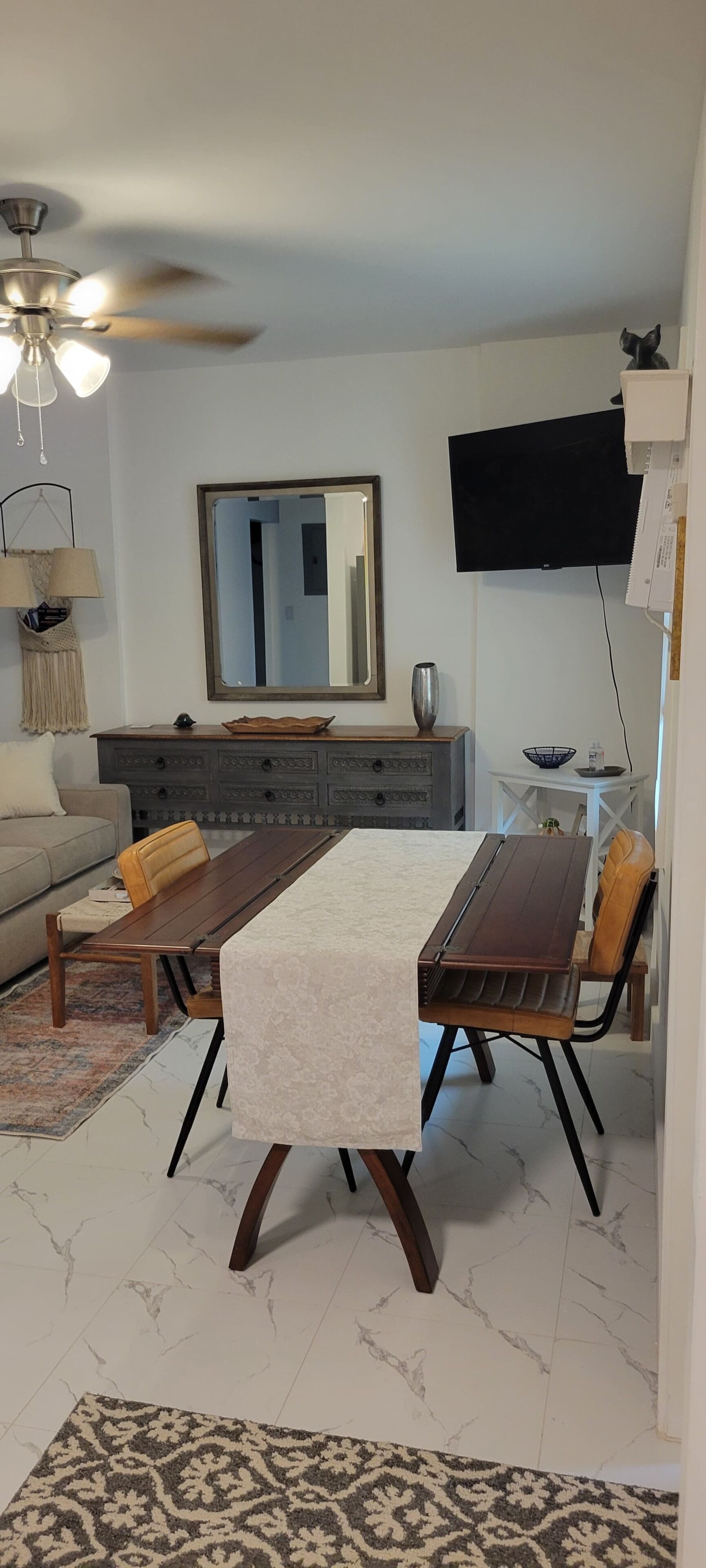 Een eetgedeelte met een tafel, stoelen, een bank, een televisie en een plafondventilator.