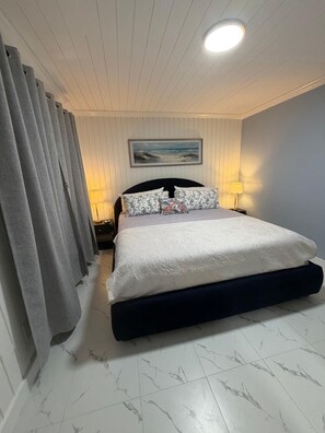 Ein Schlafzimmer mit Bett, Vorhängen, einem Gemälde und einem Nachttisch mit Lampe.