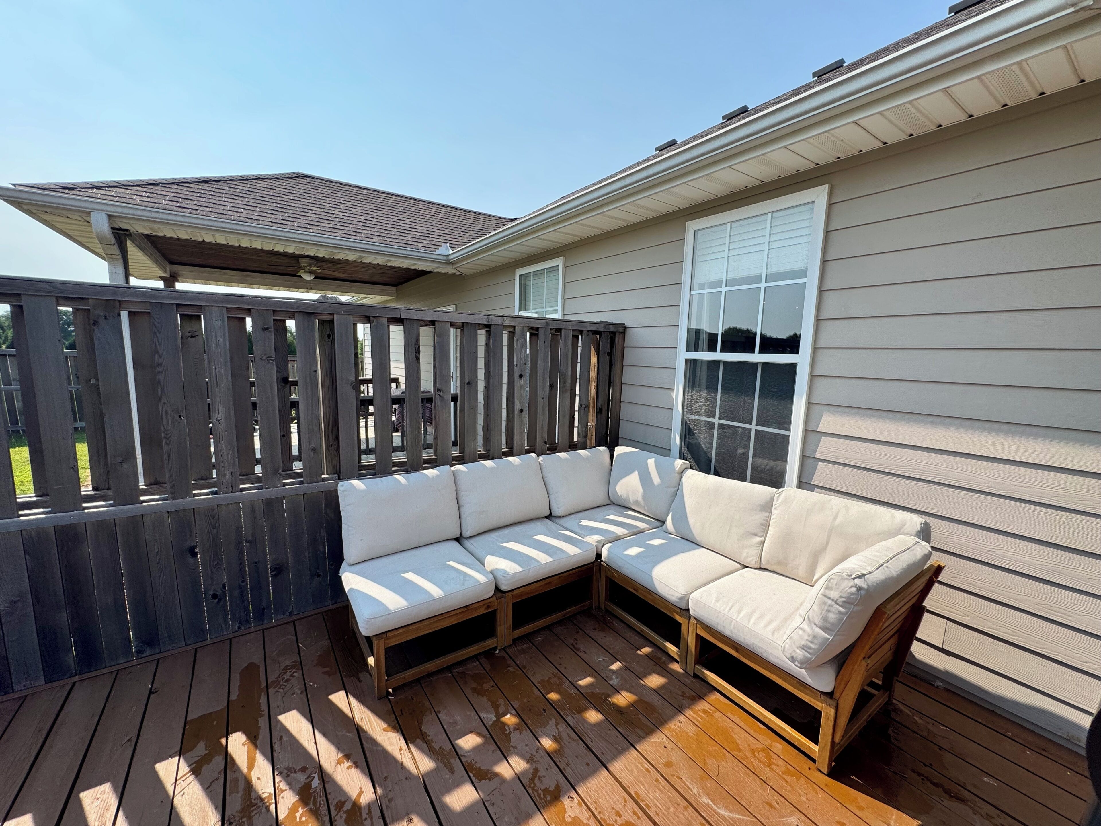 A covered deck with a wooden bench and a white cushioned sofa.