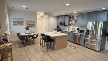 A modern kitchen with grey cabinets, stainless steel appliances, and a central island with bar stools.