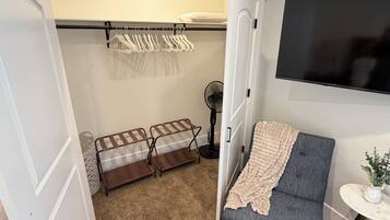 Una habitación compacta con cama, una zona de estar con manta, televisión, ventilador y perchero.