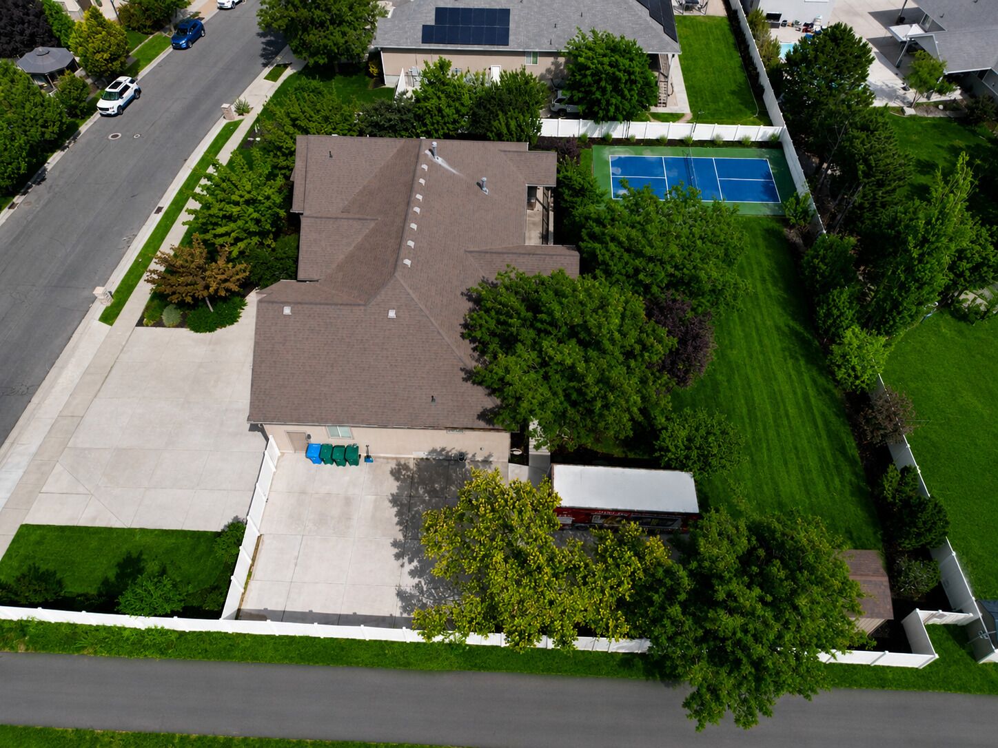Vista aérea de una zona residencial que muestra una casa, un camino de entrada, una cancha de tenis y abundante vegetación.
