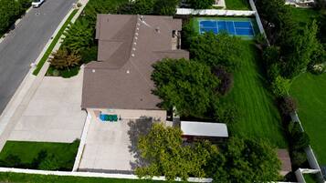 Vista aérea de una zona residencial que muestra una casa, un camino de entrada, una cancha de tenis y abundante vegetación.