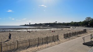 Ein Strand mit einer Holzumzäunung, einem Betonweg und blauem Himmel.